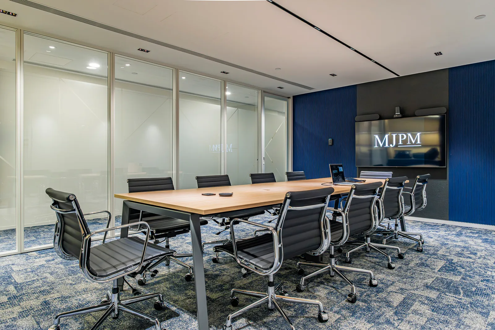 Meeting room with blue acoustic wall panels and an MJPM-branded screen